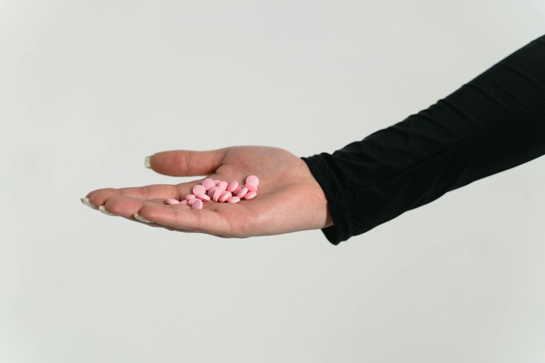 close up shot of a person holding pink pills on white background